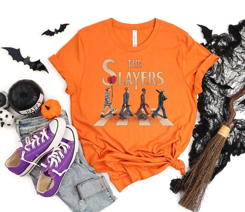 May include: Orange t-shirt with a graphic of horror movie characters walking across a crosswalk. The text "The Slayers" is above the characters.