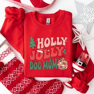 May include: Red Christmas sweatshirt with the text "HOLLY JOLLY DOG MOM" in a retro font. The sweatshirt has a green Christmas tree, a Santa hat, and a colorful ornament.
