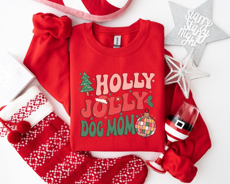 May include: Red Christmas sweatshirt with the text "HOLLY JOLLY DOG MOM" in a retro font. The sweatshirt has a green Christmas tree, a Santa hat, and a colorful ornament.