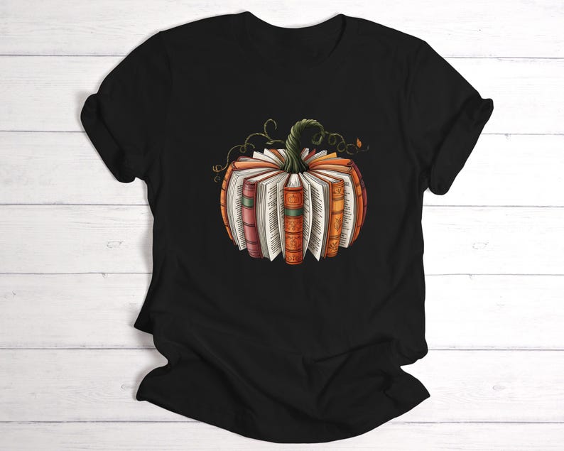May include: A black short-sleeve t-shirt featuring a central graphic of a pumpkin constructed from the spines and pages of various books. The pumpkin has a green stem with curling vines and displays books in shades of orange, red, and brown.