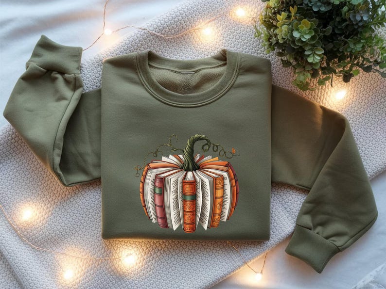 May include: An olive green crewneck sweatshirt featuring a central graphic of a pumpkin constructed from stacked, open books with colorful spines and a green stem. The sweatshirt has long sleeves with ribbed cuffs and a ribbed neckline.