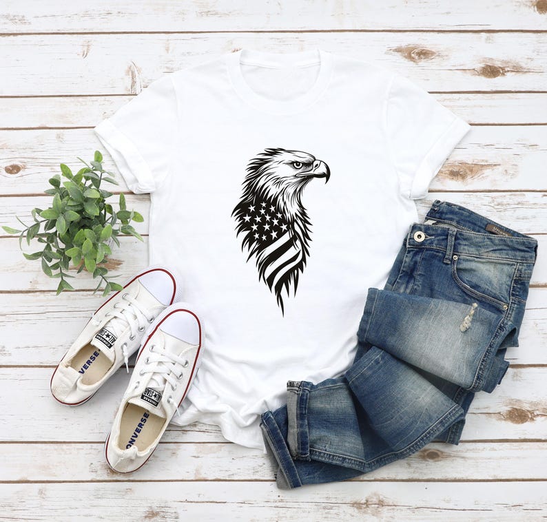 May include: White t-shirt with a black and white graphic of an eagle with the American flag on its chest.