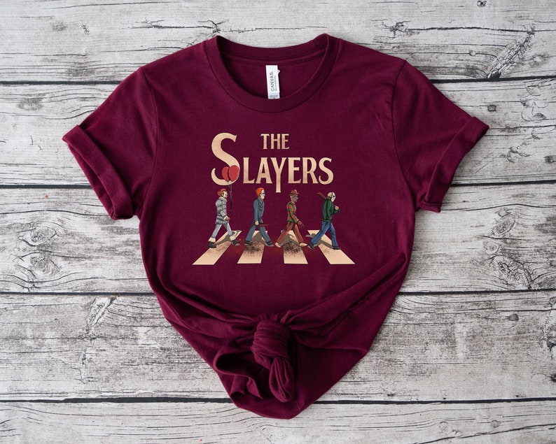 May include: Burgundy t-shirt with a graphic of four figures walking across a crosswalk, similar to the Beatles' Abbey Road album cover. The text "The Slayers" is above the figures.