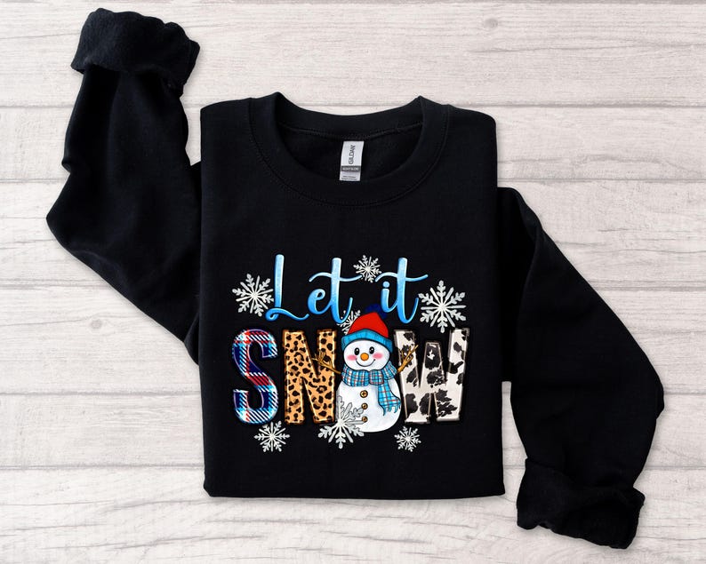 Op de afbeelding: Zwart sweatshirt met een sneeuwpop-afbeelding en de tekst "Let it snow". De sneeuwpop draagt een blauwe en witte muts en sjaal. De tekst is in wit en blauw.