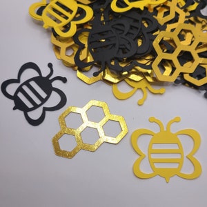 Peut inclure: Une collection de découpes de papier d'abeilles et de nids d'abeilles en noir et or. Les découpes d'abeilles ont des rayures noires et blanches et les nids d'abeilles sont dorés avec une finition pailletée.