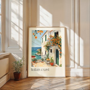 May include: A framed print of a painting depicting a white building with a balcony covered in orange flowers. The building is located on a cliff overlooking a blue body of water. The text "Italian Coast" is printed at the bottom of the print.