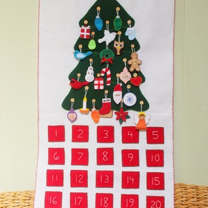 May include: A felt Christmas advent calendar shaped like a green Christmas tree with 25 numbered red squares. The tree is decorated with felt ornaments, including a bird, a snowman, a candy cane, a star, a mitten, a bell, a gift, a pear, a wreath, a gingerbread man, an owl, and a stocking.