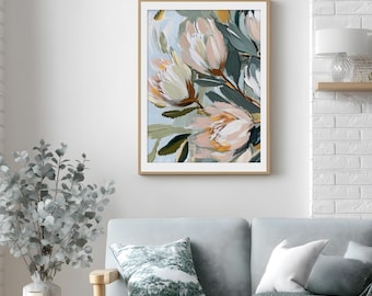 Puede incluir: Impresión artística enmarcada con flores abstractas en tonos crema, melocotón y verde sobre un fondo azul claro. La obra, en un marco dorado, cuelga de una pared blanca, sobre un sofá azul claro.