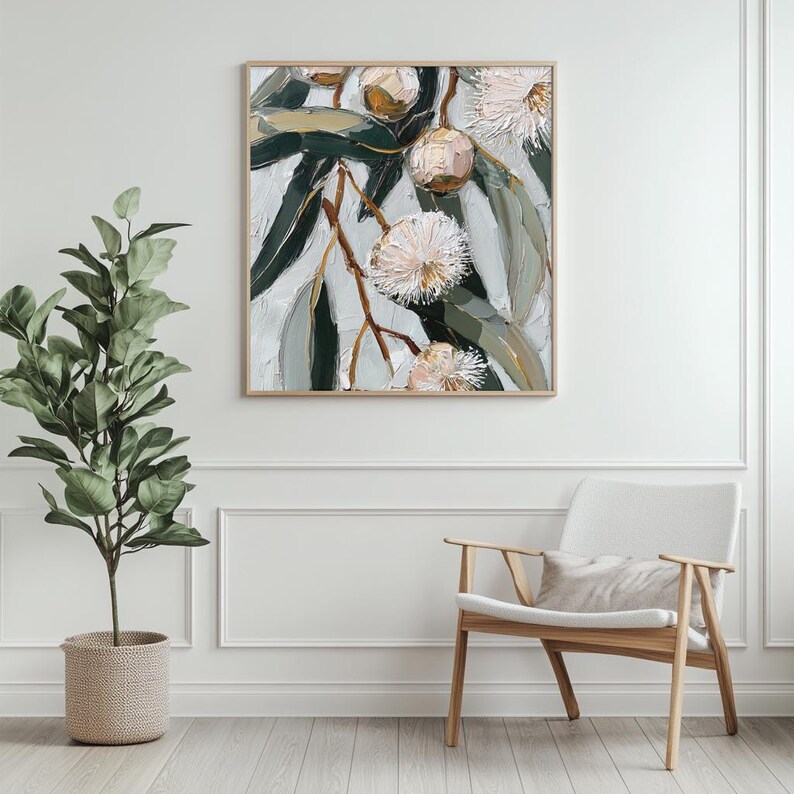 May include: An oil painting of eucalyptus blossoms and leaves in shades of green, white, and gold, framed in a light wood. The artwork hangs on a white wall above a wooden chair with a white cushion. A potted plant is in the foreground.
