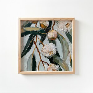 May include: Square framed painting of eucalyptus branches with green leaves and white, fluffy flowers. The artwork has a textured, impasto style, with visible brushstrokes. The frame is made of light-colored wood.