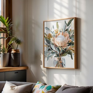 Puede incluir: Impresión artística enmarcada que presenta un arreglo floral de protea en un jarrón de cristal. La obra de arte tiene una paleta de colores suaves de melocotón, verde y blanco, con un marco de madera natural. Cuelga en una pared blanca.