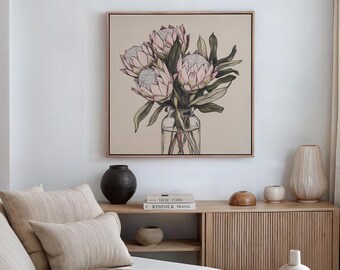 May include: A framed illustration of a bouquet of pink protea flowers in a clear glass vase. The vase is sitting on a wooden shelf with a book titled "Kinfolk Travel" and a wooden bowl.