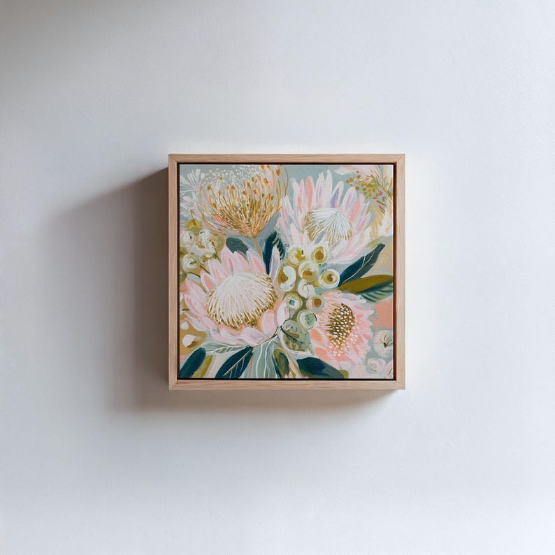 May include: Square framed floral painting featuring pink, peach, and white protea flowers with green leaves and accents. The artwork is set against a light blue-green background and framed in natural wood.