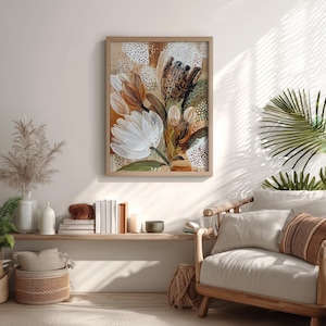以下が含まれることがあります： 白、茶色、緑色の筆致が特徴の、額装された抽象的な花の絵画。このアートワークは、ニュートラルな背景に、大きく様式化された花と葉を描いています。この絵画は明るい色の木製フレームに収められており、部屋に自然な暖かさを加えています。