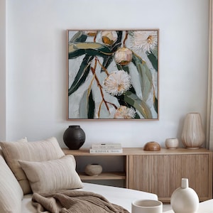 May include: Square framed painting of a botanical scene. The artwork features a close-up of eucalyptus branches with green leaves and white, fluffy flowers. The painting has a textured, impasto style with a neutral color palette.