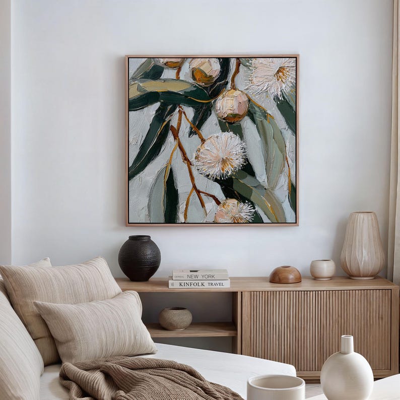 May include: Square framed painting of a botanical scene. The artwork features a close-up of eucalyptus branches with green leaves and white, fluffy flowers. The painting has a textured, impasto style with a neutral color palette.