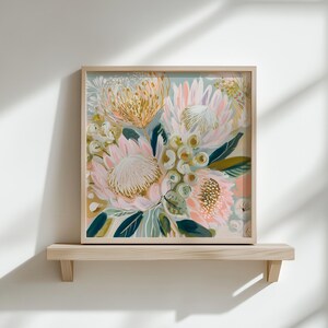 May include: Square framed floral art print featuring a bouquet of pink, yellow, and white flowers with green leaves. The artwork is displayed on a light wood shelf against a white wall. The flowers have a textured appearance.