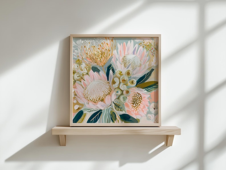 May include: Square framed floral art print featuring a bouquet of pink, yellow, and white flowers with green leaves. The artwork is displayed on a light wood shelf against a white wall. The flowers have a textured appearance.