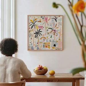 Puede incluir: Una impresión artística enmarcada que presenta un paisaje abstracto colorido con palmeras y edificios. La obra de arte, en un marco de madera, cuelga de una pared blanca. Un cuenco de madera con fruta descansa sobre una mesa de madera.