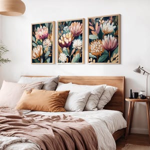 Puede incluir: Tres impresiones artísticas florales enmarcadas con flores estilo acuarela en tonos rosa, blanco y naranja sobre un fondo oscuro. La obra de arte se exhibe sobre una cama con cabecero de madera, almohadas y una manta marrón.