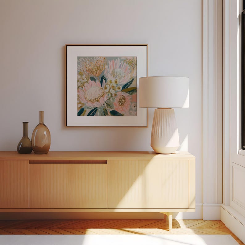 May include: A framed floral art print with pink and yellow flowers hangs above a light wood cabinet. A white lamp with a textured base sits on the cabinet. Two brown glass vases are also on the cabinet.