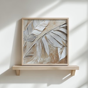 May include: A framed painting of stylized beige and white leaves in a textured style. The painting is on a light wood shelf against a white wall.