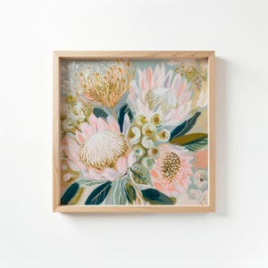 May include: Square framed floral art print featuring a bouquet of protea flowers in shades of pink, gold, and green. The artwork is set against a soft, light background, and the frame is made of natural wood.