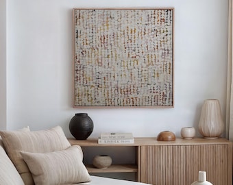Könnte beinhalten: Ein quadratisches abstraktes Gemälde mit hellem Holzrahmen hängt über einem Holzschrank. Das Gemälde zeigt ein Muster aus kleinen, farbigen Punkten. Dekorative Vasen und Bücher sind auf dem Schrank angeordnet. Beige Kissen und eine Decke liegen auf dem Bett.