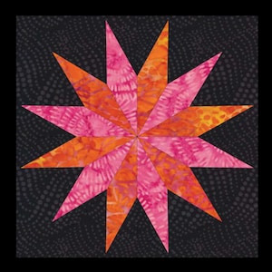May include: A fabric star quilt block featuring a vibrant starburst design. The star is composed of orange and pink batik fabric, set against a dark gray background. The star's points radiate from the center, creating a striking visual effect.