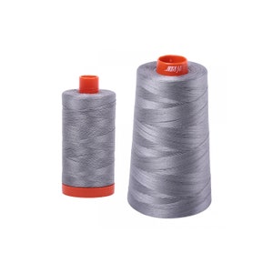 May include: Two spools of gray thread with orange bases. The spool on the left is cylindrical, while the one on the right is conical. The thread is tightly wound, and the spools are set against a white background.