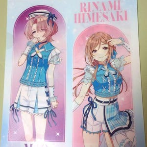 May include: A clear plastic folder featuring two anime-style illustrations of young women. The women are dressed in blue and white outfits. The text "RINAMI HIMESAKI" and "MAO ARIMURA" are visible on the folder. The background is a light pink and purple.