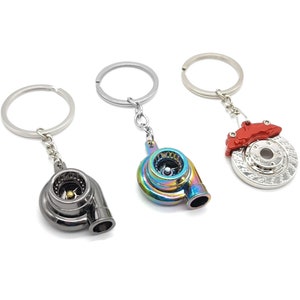 May include: Three different car part keychains. One is a silver brake rotor with a red caliper. The other two are turbochargers, one is black and the other is iridescent.