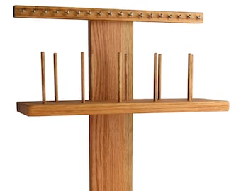 May include: A wooden jewelry stand with multiple pegs for hanging earrings and necklaces. The stand has two shelves and a base with additional pegs for storing jewelry.