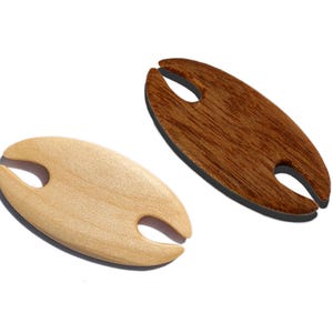 May include: Two wooden wine glass holders. One is light-colored, the other is dark brown. Each has an oval shape with a slot for the stem of a wine glass. The holders are on a white background.