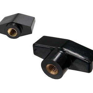 May include: Two black T-knobs with brass-colored threaded inserts. The knobs have a rectangular shape with rounded edges and a smooth, glossy finish. The background is plain white.