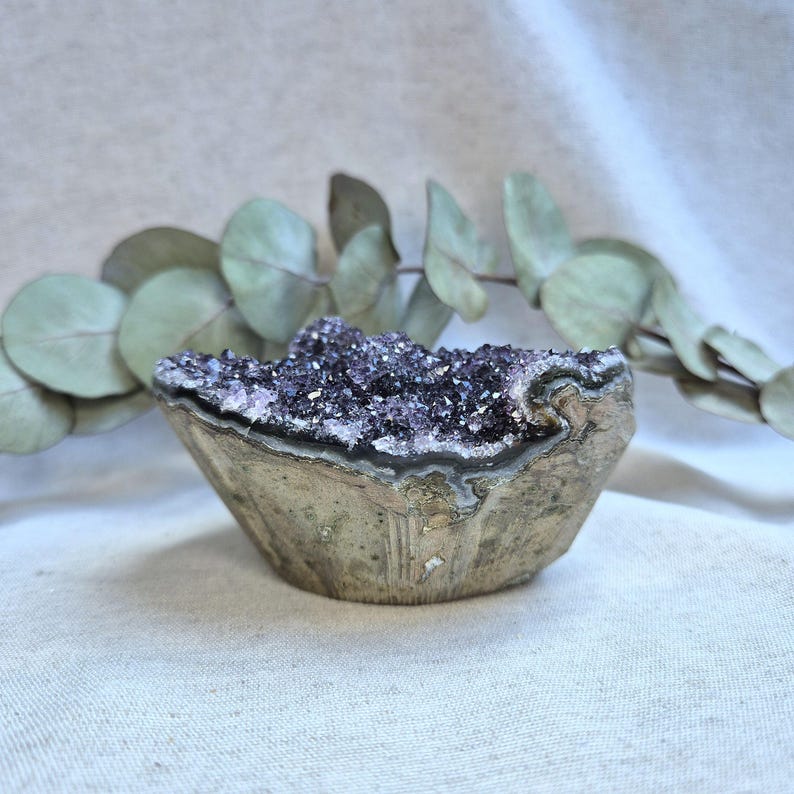 Pu&ograve; includere: Una geode di ametista viola con un esterno naturale e ruvido e un interno liscio e lucido. La geode &egrave; piena di piccoli cristalli scintillanti.