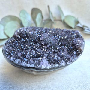 Pu&ograve; includere: Una grande geode di ametista con una formazione di cristalli viola e bianchi. La geode &egrave; liscia e lucida, con una forma naturale e organica.