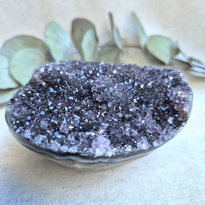 Pu&ograve; includere: Una grande geode di ametista con una formazione di cristalli viola e bianchi. La geode &egrave; liscia e lucida, con una forma naturale e organica.