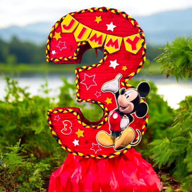 May include: A red and yellow Mickey Mouse themed pi&ntilde;ata shaped like the number 3. The pi&ntilde;ata has a banner that says "JIMMY" and features Mickey Mouse in a red and yellow outfit.