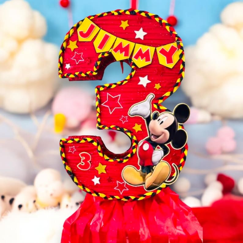May include: Red and yellow Mickey Mouse themed pi&ntilde;ata shaped like the number 3. The pi&ntilde;ata has a banner that says "JIMMY" and stars.
