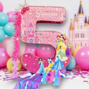May include: Pink number 5 piñata with a princess theme, featuring a castle, princess illustrations, and the name "Gianna". The piñata is decorated with stars, a crown, and colorful streamers, surrounded by balloons.