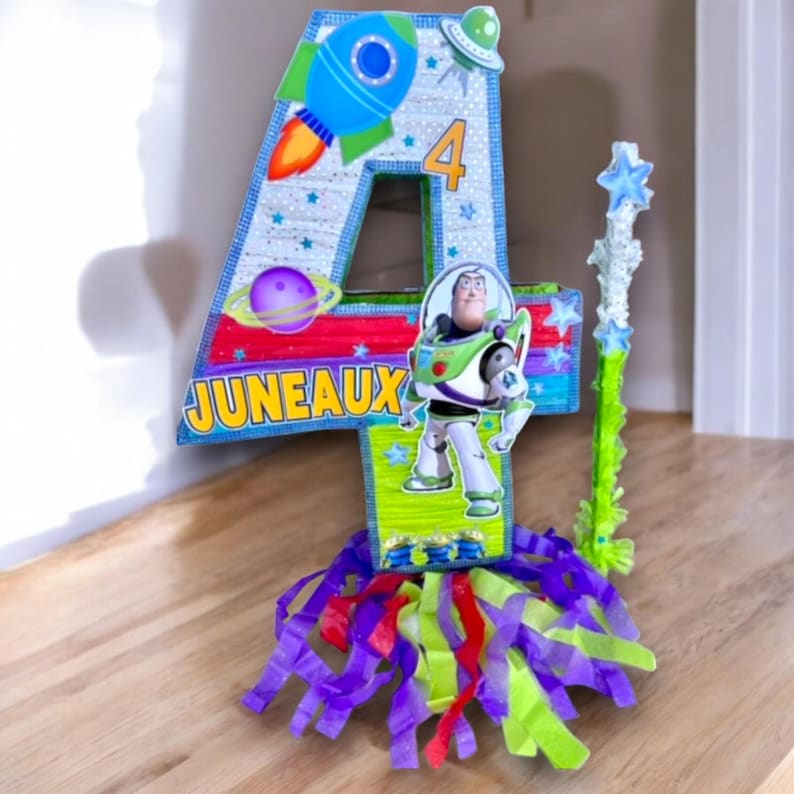 Puede incluir: Una colorida pi&ntilde;ata con forma de n&uacute;mero cuatro con tem&aacute;tica espacial. Presenta un cohete, planetas, estrellas y una imagen de Buzz Lightyear de la pel&iacute;cula Toy Story. La pi&ntilde;ata est&aacute; decorada con serpentinas verdes, azules, rojas y moradas.