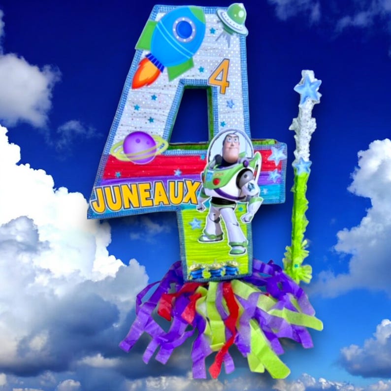Puede incluir: Una pi&ntilde;ata de n&uacute;mero cuatro azul y verde con tem&aacute;tica espacial. La pi&ntilde;ata presenta un cohete, planetas, estrellas y un personaje de la pel&iacute;cula Toy Story. La pi&ntilde;ata tiene el nombre "JUNEAUX" escrito en ella.
