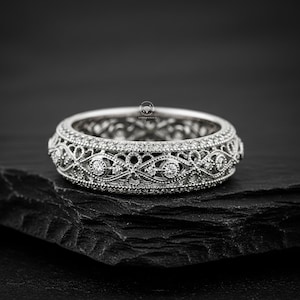 以下が含まれることがあります： 精巧なフィリグリーデザインのシルバーリング。リングには、詳細なパターンの中に小さな輝く石がセットされています。バンドは連続したループで、ジュエリーの職人技を表現しています。