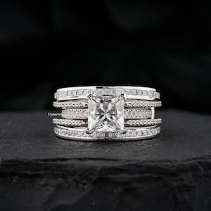 May include: A silver ring with a large square-shaped diamond surrounded by smaller diamonds. The ring has multiple bands with smaller diamonds.