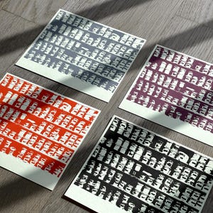 May include: Four square cards with a repeating pattern of white and gray, white and red, white and black, and white and purple. The cards are printed with a pattern of small squares.