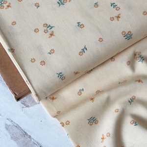 May include: Cream colored fabric with a repeating pattern of small orange flowers and green leaves with a small bee in each cluster of flowers.