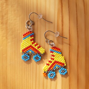 May include: A pair of beaded roller skate earrings. The earrings are made with colorful beads in shades of yellow, red, blue, and orange. The earrings are attached to silver hooks.