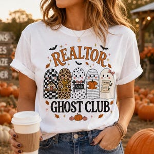 May include: A white t-shirt featuring a graphic of five ghosts with various patterns, including a house, a leopard print, a sold sign, a pumpkin, and a contract. The text reads REALTOR GHOST CLUB in orange and black, surrounded by small bats and leaves.