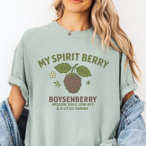 May include: A light green t-shirt with the text "MY SPIRIT BERRY" above a boysenberry graphic. Below the graphic, the text reads "BOYSENBERRY MELLOW, BOLD, LOW-KEY & A LITTLE DARING". The shirt is a relaxed fit.